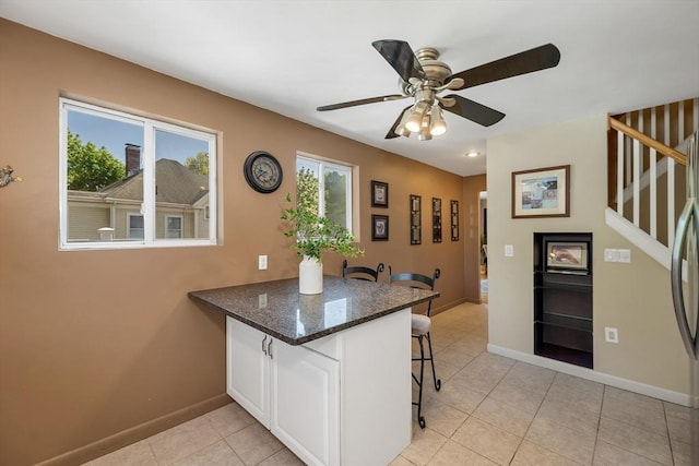 kitchen with a kitchen breakfast bar, baseboards, a peninsula, a ceiling fan, and light tile patterned floors