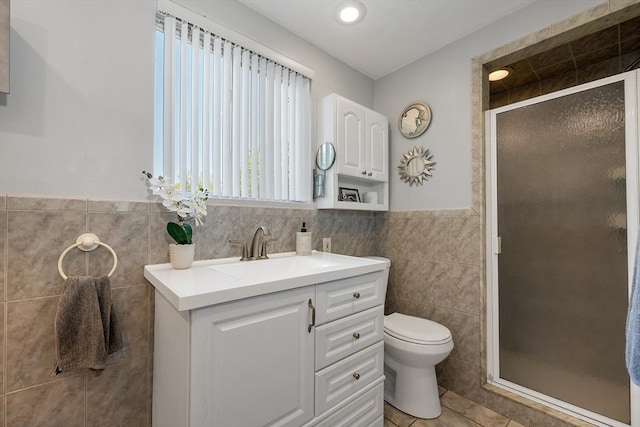 bathroom with tile walls, a shower stall, toilet, vanity, and tile patterned flooring