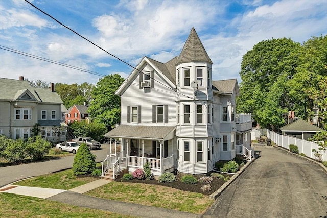 victorian home featuring a porch, fence, and roof with shingles