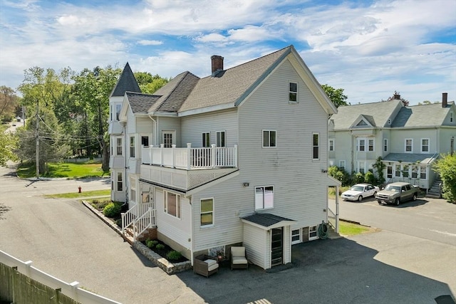 back of property with a balcony, a chimney, and roof with shingles