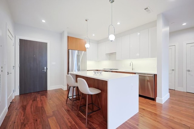 kitchen with appliances with stainless steel finishes, hanging light fixtures, a center island, white cabinets, and sink