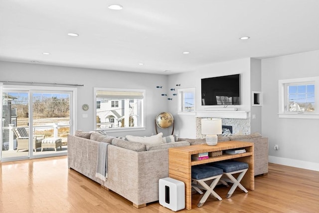living room featuring recessed lighting, baseboards, a stone fireplace, and light wood-style flooring
