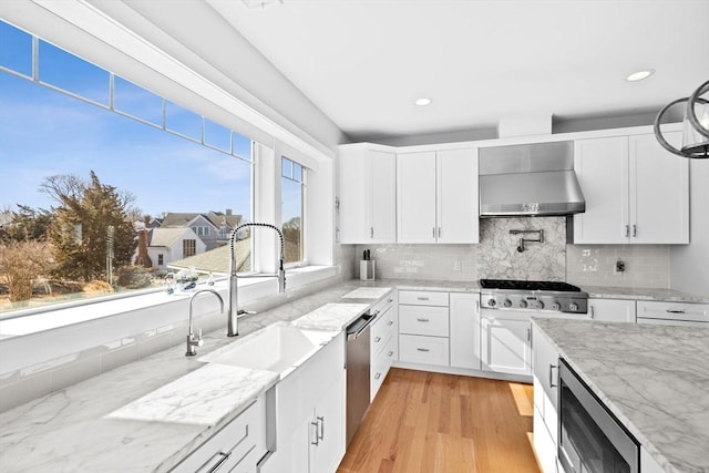 kitchen featuring white cabinetry, wall chimney range hood, light wood finished floors, and appliances with stainless steel finishes