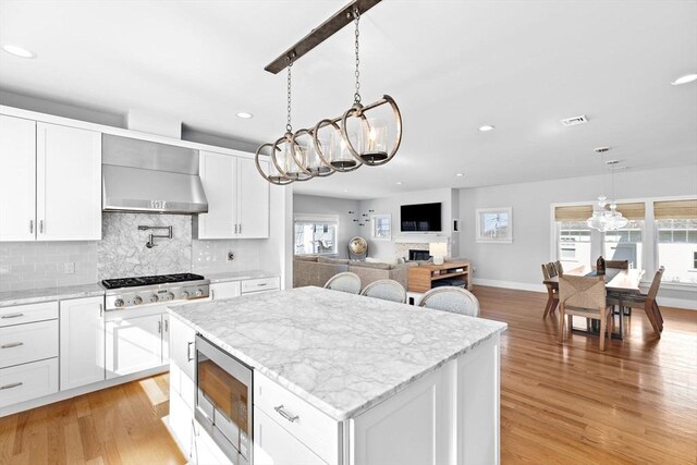 kitchen featuring wall chimney exhaust hood, stainless steel appliances, light wood finished floors, and a chandelier