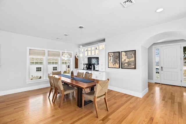 dining room featuring visible vents, arched walkways, baseboards, and light wood finished floors