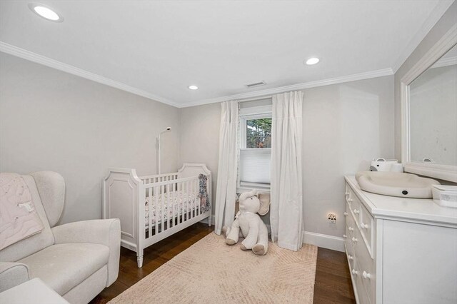 bedroom featuring dark hardwood / wood-style floors, crown molding, and a nursery area