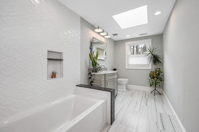 bathroom featuring vanity, toilet, a bath, and a skylight