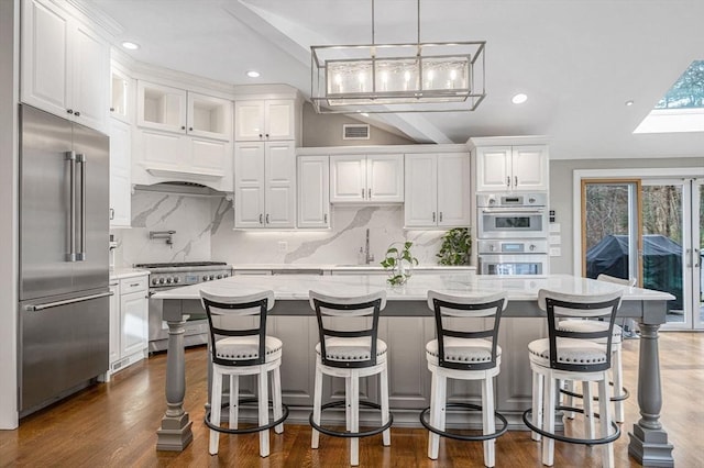 kitchen with high quality appliances, white cabinetry, and an island with sink