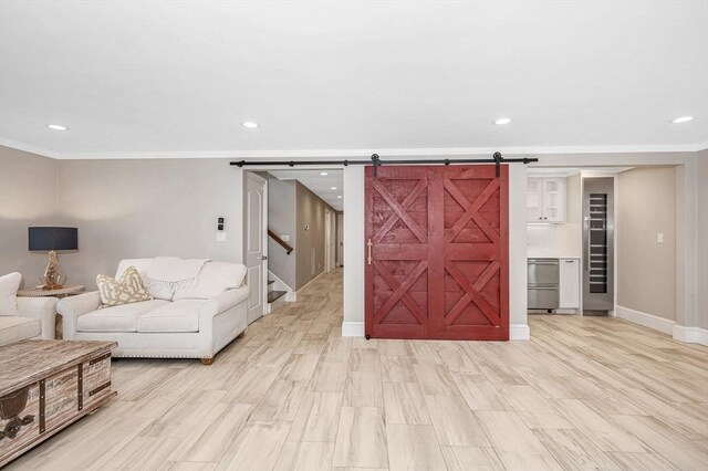 living room with a barn door, light wood-type flooring, and ornamental molding