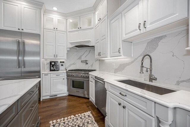 kitchen with light stone countertops, dark hardwood / wood-style flooring, high end appliances, sink, and white cabinets