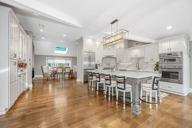 kitchen with a center island, tasteful backsplash, a kitchen bar, vaulted ceiling with skylight, and white cabinets