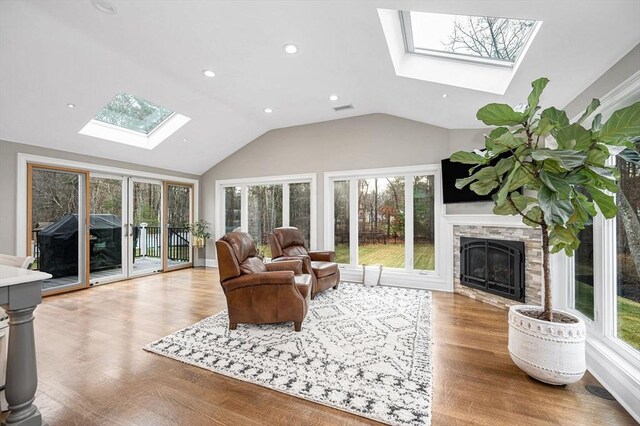 living room featuring light wood-type flooring, vaulted ceiling, and a stone fireplace