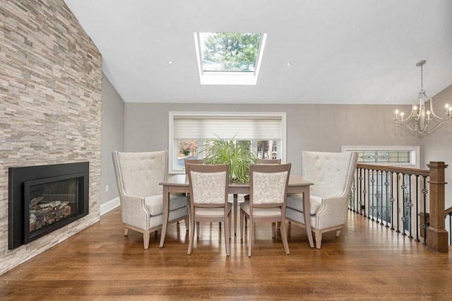 dining room with a stone fireplace, lofted ceiling with skylight, hardwood / wood-style floors, and an inviting chandelier