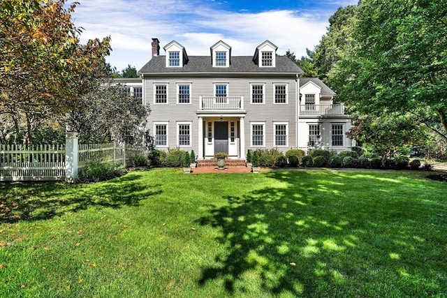 colonial-style house featuring a balcony, fence, and a front yard