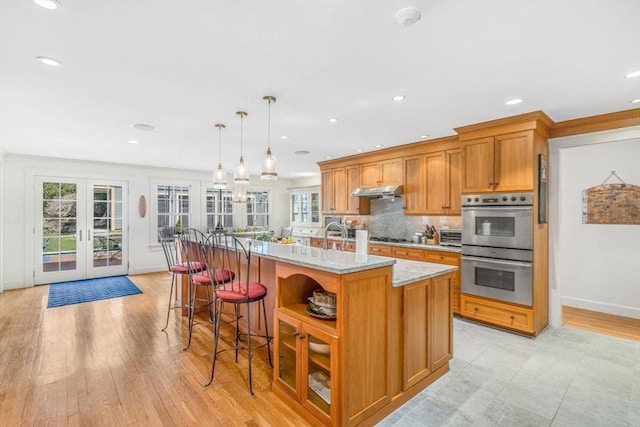 kitchen with tasteful backsplash, brown cabinetry, a kitchen island with sink, stainless steel double oven, and french doors