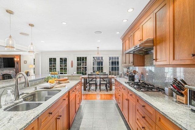 kitchen with under cabinet range hood, a sink, brown cabinets, decorative light fixtures, and stainless steel gas stovetop