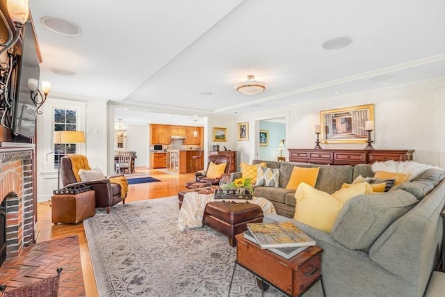 living room featuring baseboards, light wood finished floors, ornamental molding, a brick fireplace, and a tray ceiling