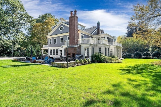 back of house with a chimney, a patio area, a lawn, and a balcony