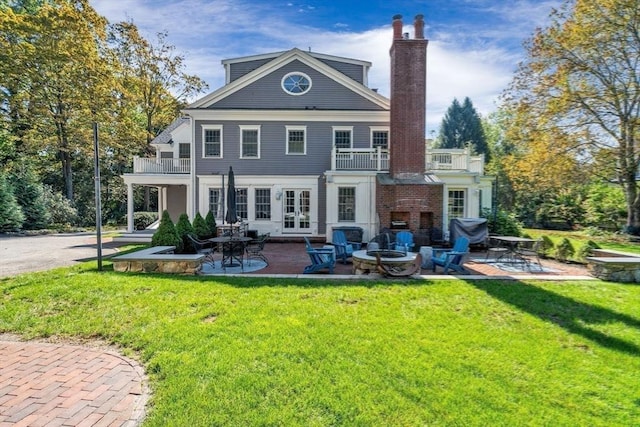 rear view of property featuring a balcony, a lawn, french doors, and a patio