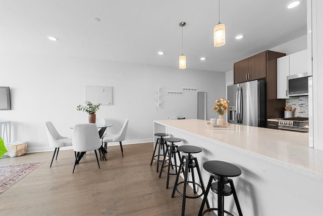 kitchen with recessed lighting, a breakfast bar, light wood-style flooring, baseboards, and appliances with stainless steel finishes