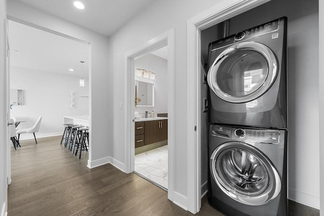 laundry room featuring recessed lighting, dark wood-style flooring, laundry area, baseboards, and stacked washer / dryer