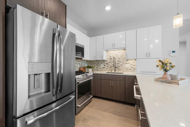 kitchen with tasteful backsplash, light wood-style flooring, stainless steel appliances, a sink, and white cabinetry