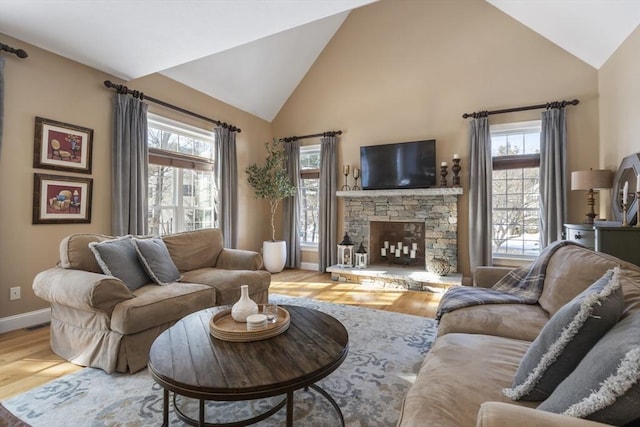 living room with hardwood / wood-style flooring, a stone fireplace, high vaulted ceiling, and a wealth of natural light