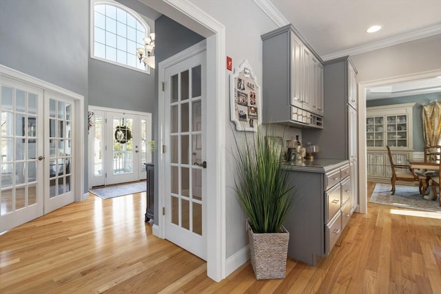 bar featuring french doors, gray cabinetry, an inviting chandelier, light wood-type flooring, and ornamental molding