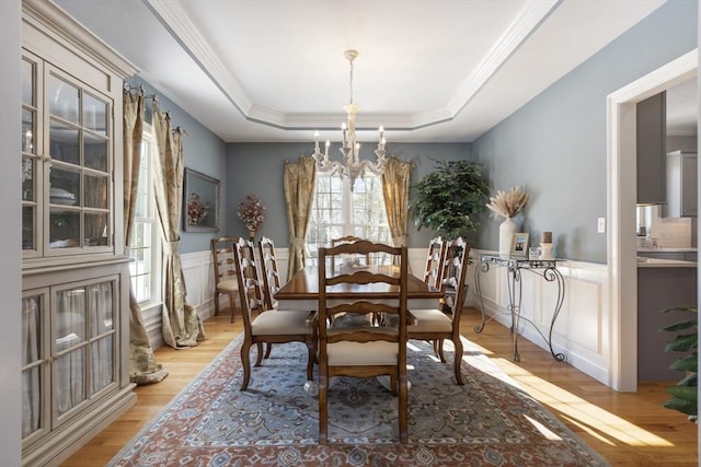 dining area featuring crown molding, a raised ceiling, light hardwood / wood-style flooring, and a notable chandelier