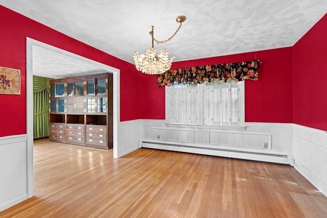 unfurnished dining area featuring wainscoting, a baseboard radiator, a notable chandelier, and wood finished floors