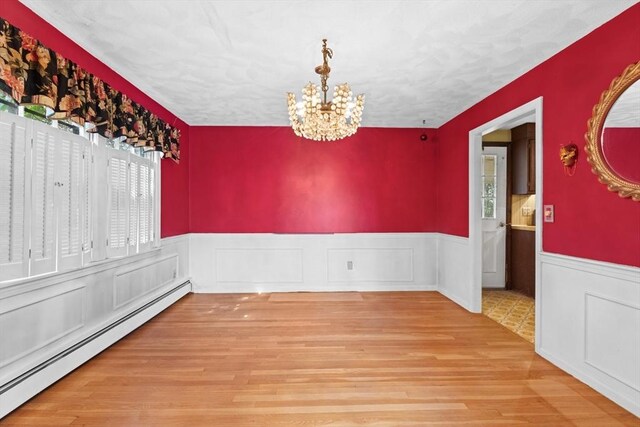 unfurnished dining area with a baseboard heating unit, wood finished floors, a notable chandelier, and wainscoting