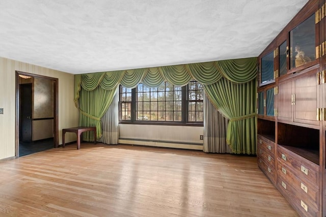 unfurnished living room with baseboard heating, a textured ceiling, and light wood finished floors