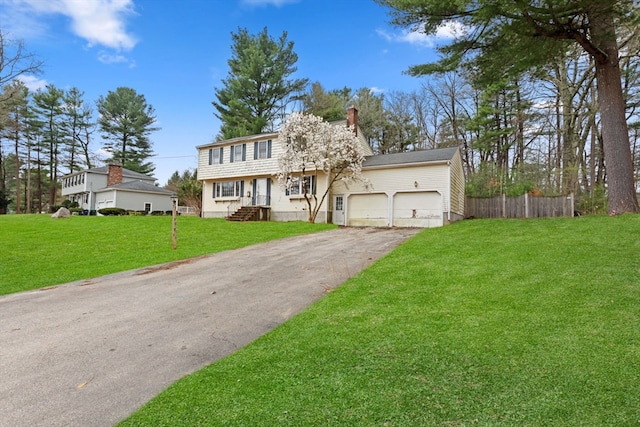 colonial-style house with a chimney, aphalt driveway, an attached garage, fence, and a front yard