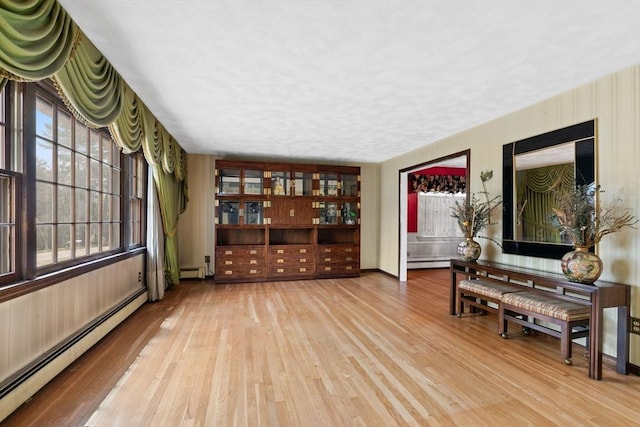 sitting room with a baseboard heating unit, wood finished floors, and baseboards