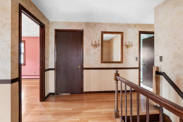 corridor featuring light wood finished floors, an upstairs landing, and wallpapered walls