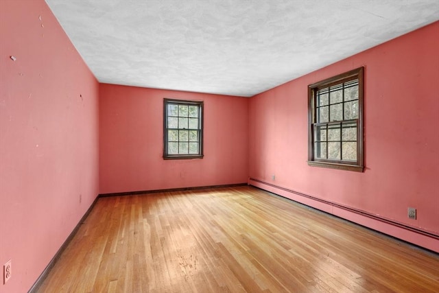spare room featuring a baseboard heating unit, baseboards, a textured ceiling, and hardwood / wood-style flooring