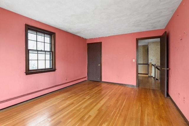 spare room with baseboard heating, baseboards, and light wood-style floors