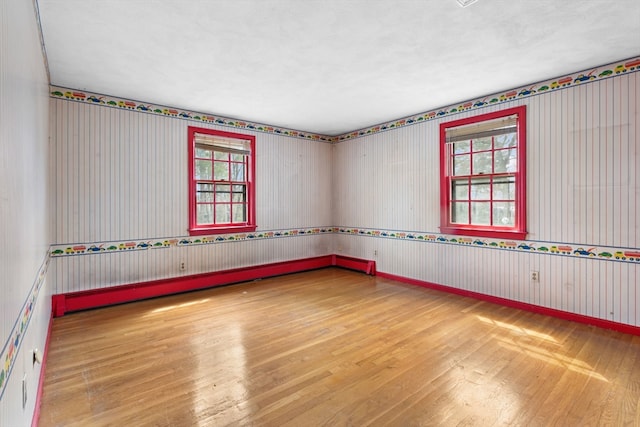 spare room with wallpapered walls and hardwood / wood-style flooring