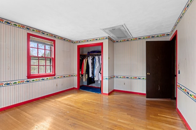 unfurnished bedroom with wallpapered walls, wood finished floors, a closet, baseboards, and attic access