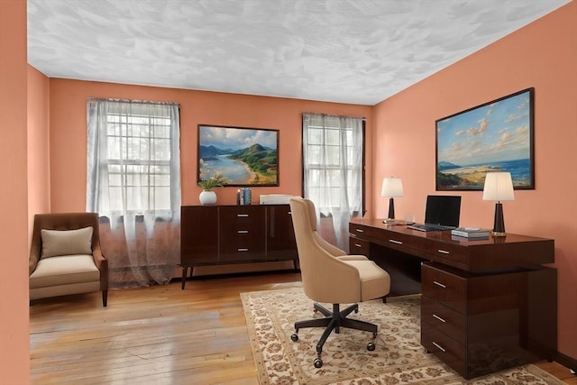 office area with a baseboard heating unit, a textured ceiling, and light wood finished floors