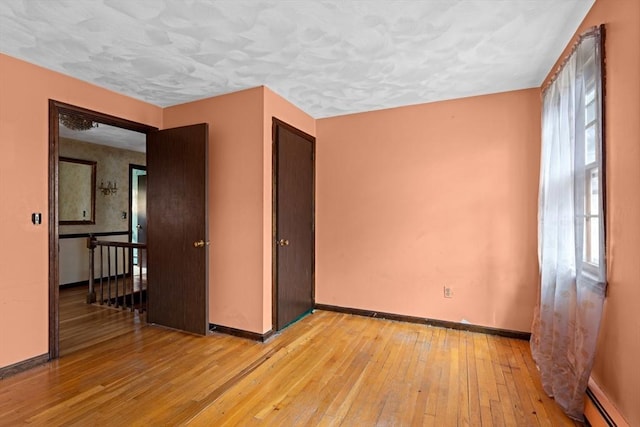 empty room with a baseboard radiator, baseboards, light wood-style floors, and a textured ceiling