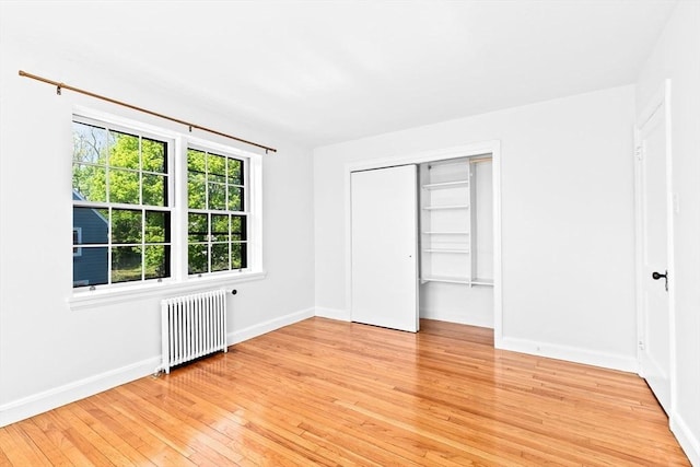 unfurnished bedroom with radiator, light wood-style floors, baseboards, and a closet