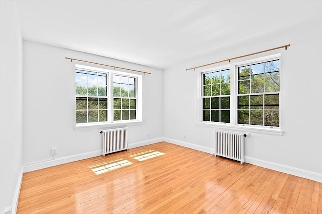 empty room with radiator heating unit, light wood-style floors, and baseboards