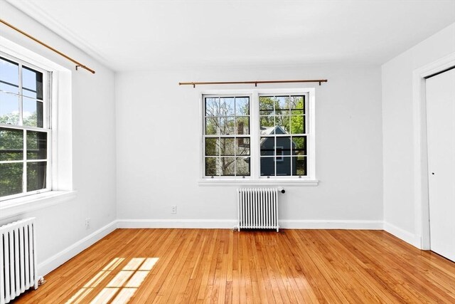 spare room with radiator heating unit, light wood-style flooring, and baseboards