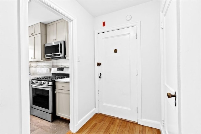kitchen with stainless steel appliances, decorative backsplash, light countertops, gray cabinets, and baseboards