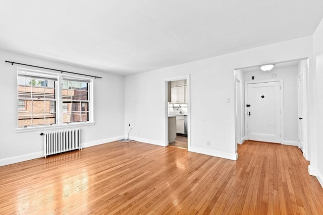 unfurnished room featuring radiator heating unit, light wood finished floors, and baseboards