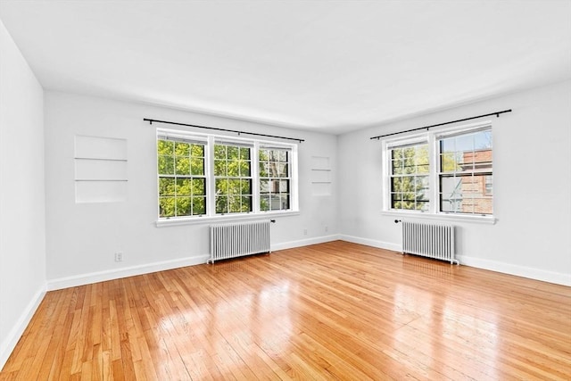empty room with radiator heating unit, healthy amount of natural light, and light wood-style floors