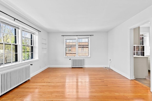 empty room featuring radiator, light wood-style floors, and baseboards