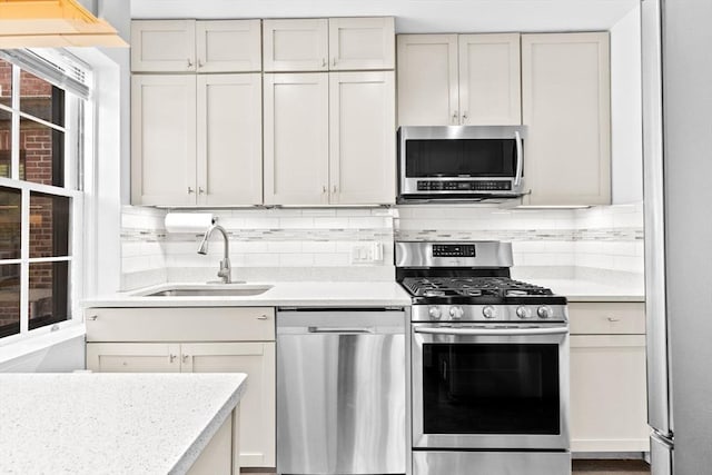 kitchen featuring appliances with stainless steel finishes, a sink, light countertops, and backsplash