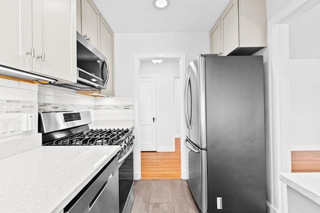 kitchen with stainless steel appliances, decorative backsplash, light stone counters, white cabinets, and baseboards